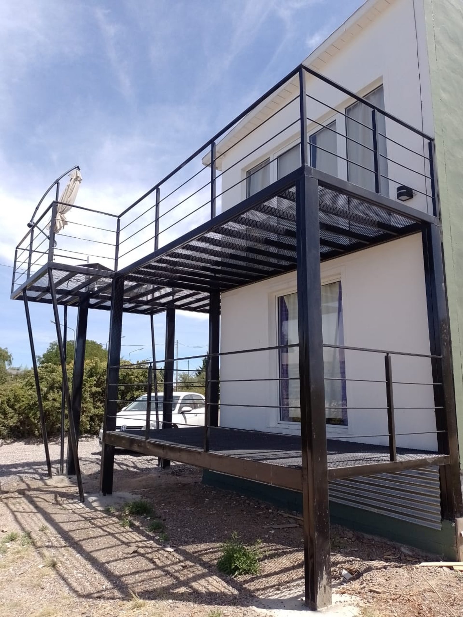 balcón metálico negro moderno frente a casa blanca — proyecto CABAÑA LAUTARO, por Estudio de Arquitectura - Verónica Sirhan , en Las Grutas